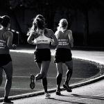 Black and white back view of unrecognizable fit female runners in sportswear running during track and field competition
